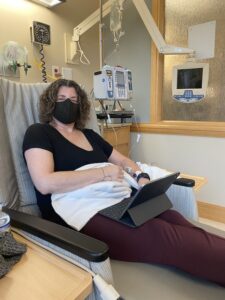 Lisa in armchair, wearing mask, getting chemo, with iPad on lap