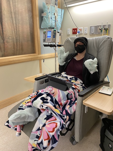 Lisa in an infusion chair with cooler packs on her hands and feet